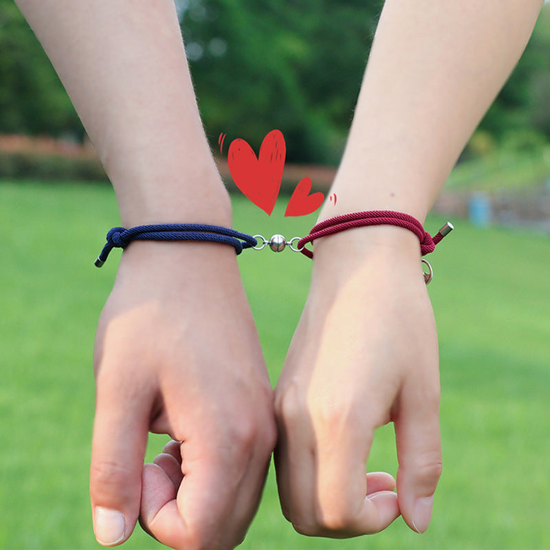 Two hands holding each other with blue and red New Alloy Eachother Couple Bracelet against a green outdoor background.